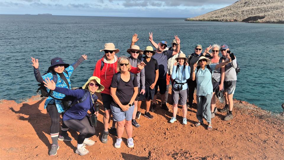 Grupo de viajeros saludando sobre arena roja frente al mar