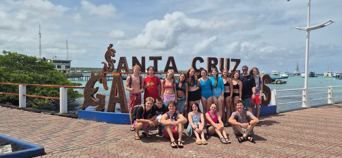 Grupo de viajeros frente al letrero de Santa Cruz en el muelle de Puerto Ayora